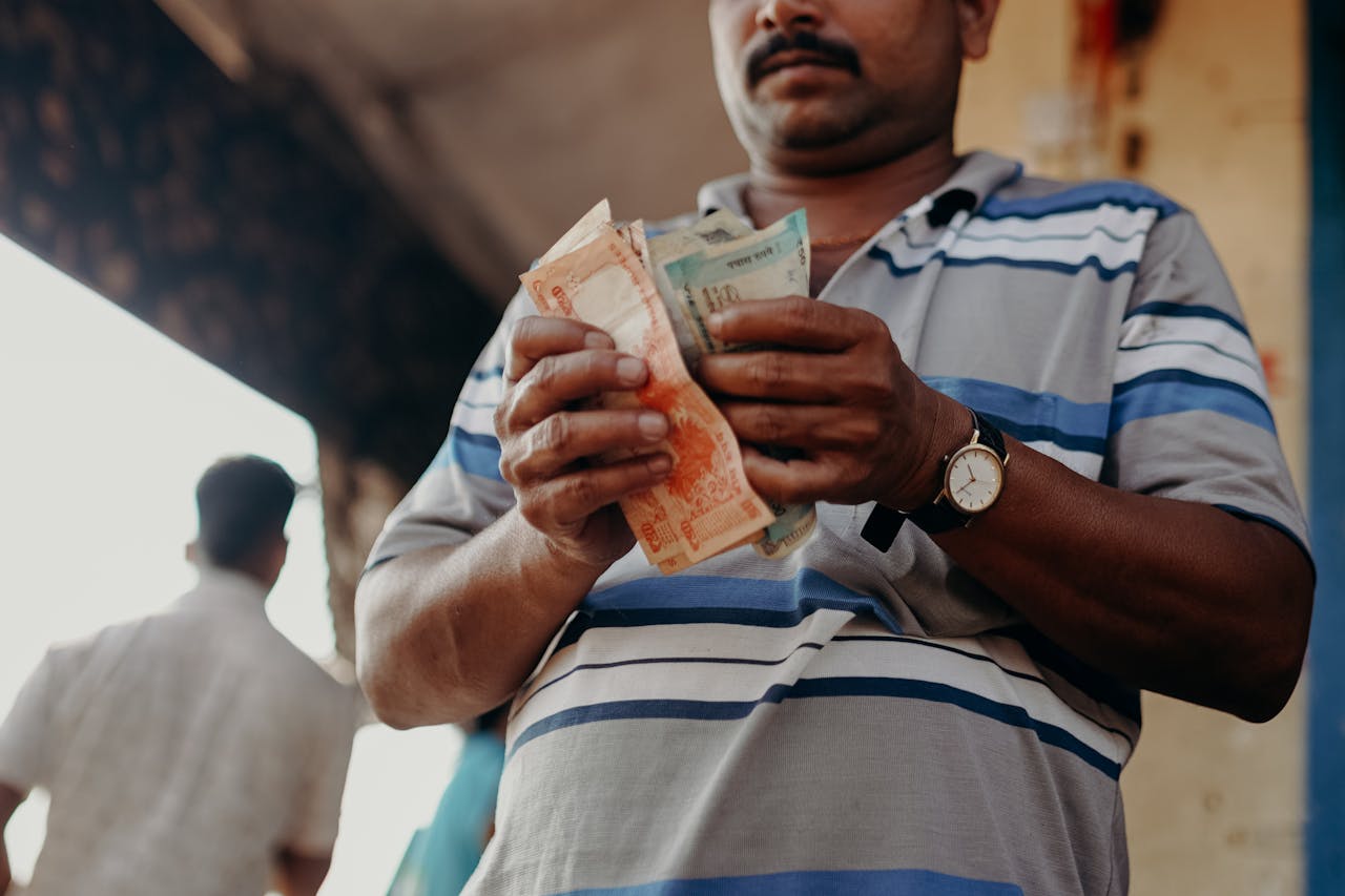 services-03 Man in Indian market counting rupee notes, showcasing daily street commerce.